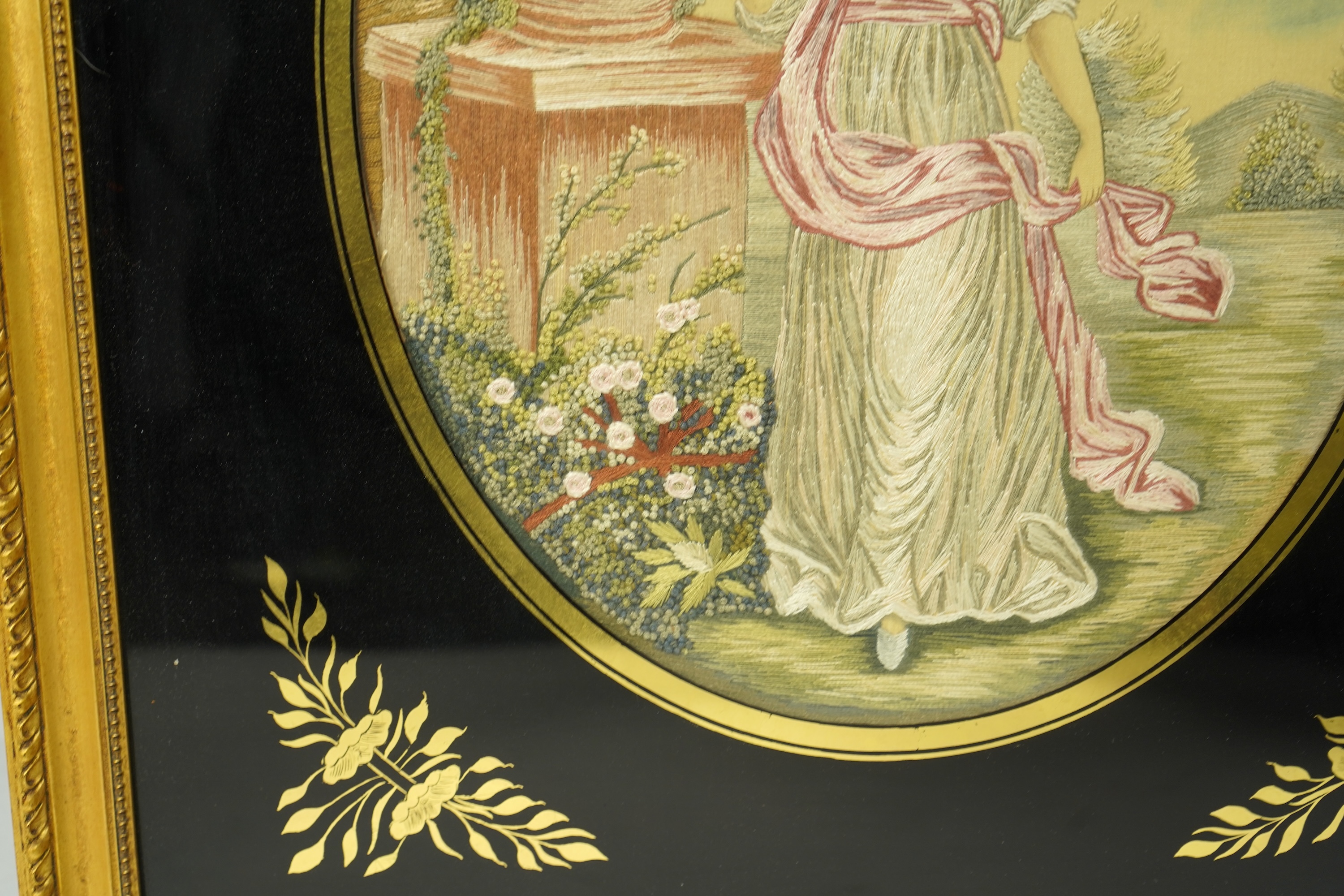 A pair of early 20th century oval silk embroideries of ladies standing by classical stone urns in a garden. Worked in pastel shades in silk using mostly stem stitch. Their faces, arms, hands and back ground silk hand pai